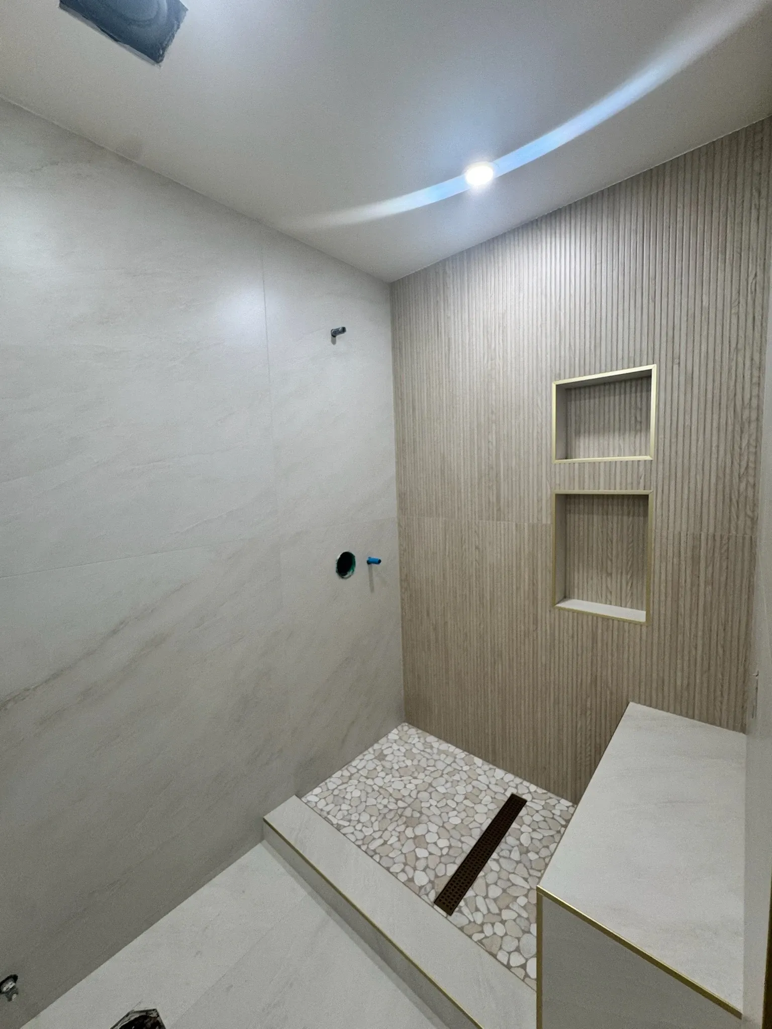 Spa-style shower with travertine walls, bench, and pebble floor