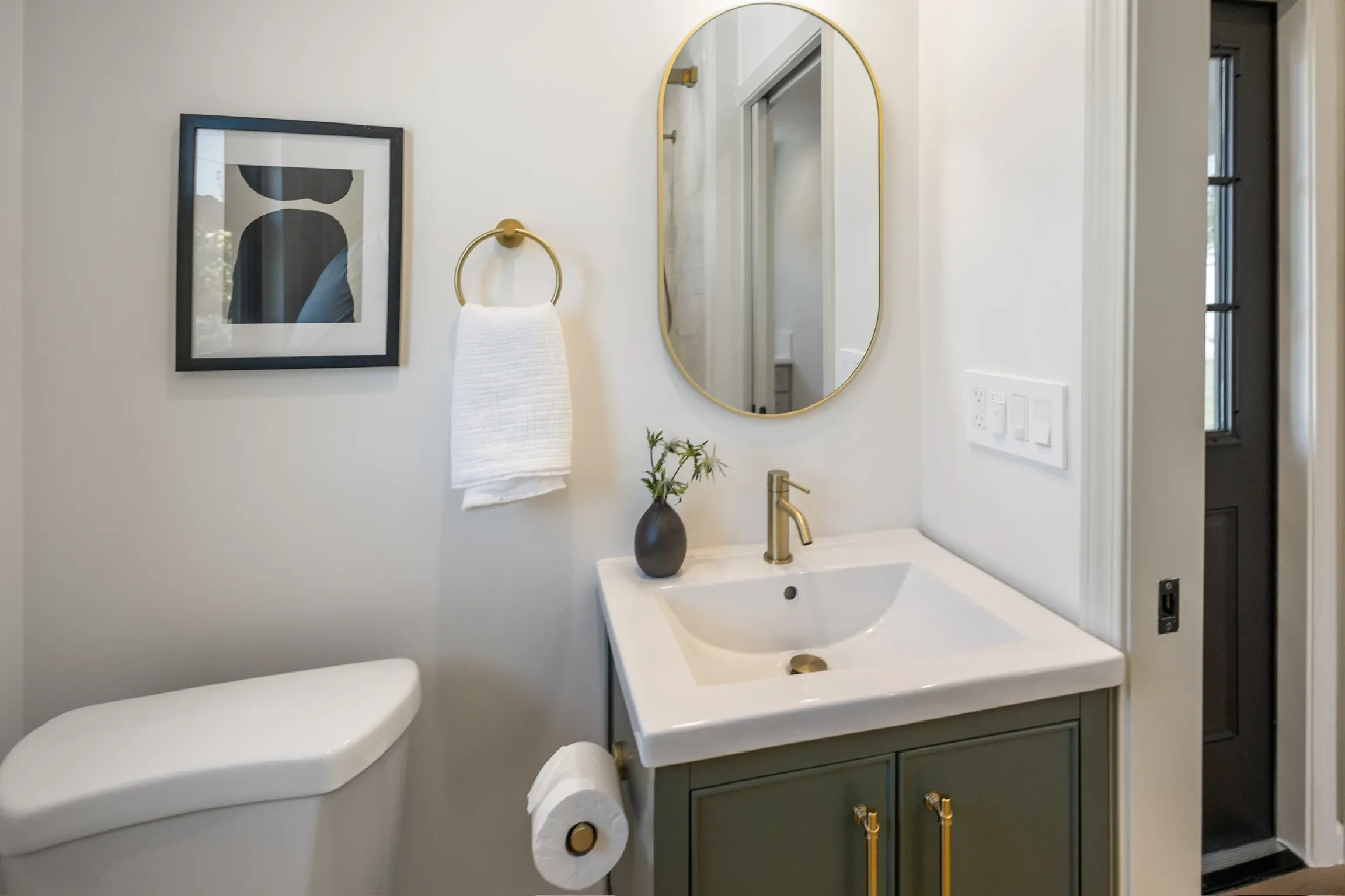 Powder room with green vanity, brass fixtures, and oval mirror