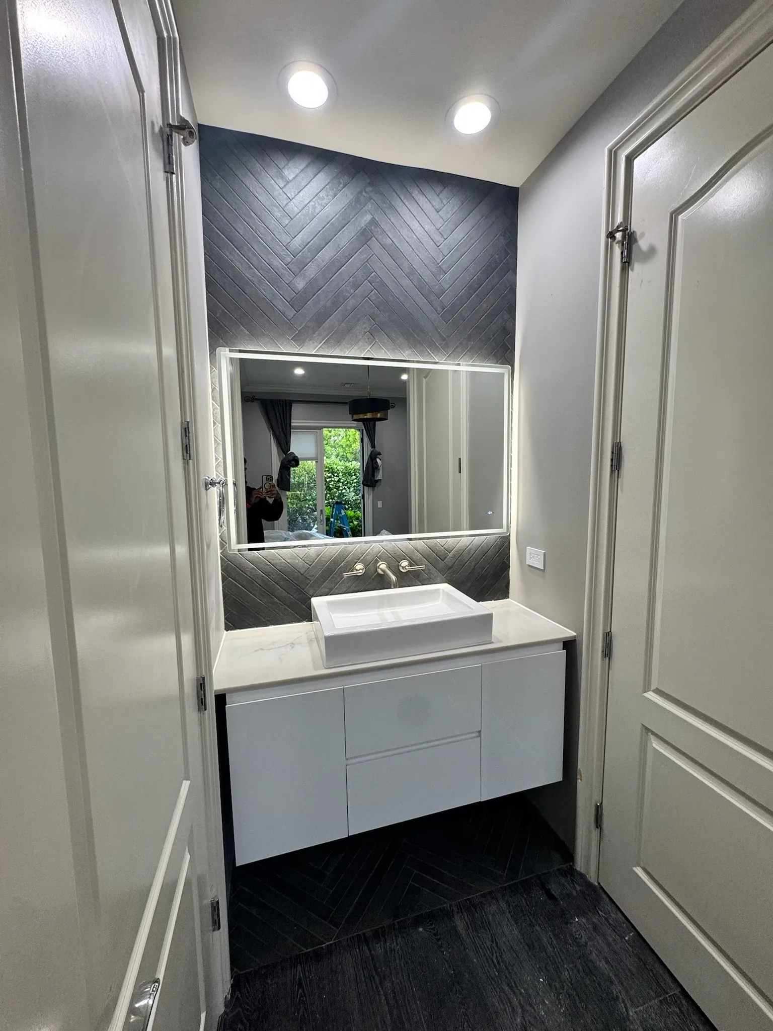 Modern bathroom with dark herringbone feature wall and backlit mirror